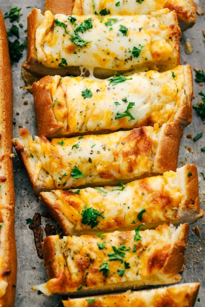 Cheesy garlic bread is so simple to make with loads of cheese and that soft bread on the inside with the crunchy crust on the outside. This is a family favorite for sure!ย Sliced cheesy garlic bread on a pan.