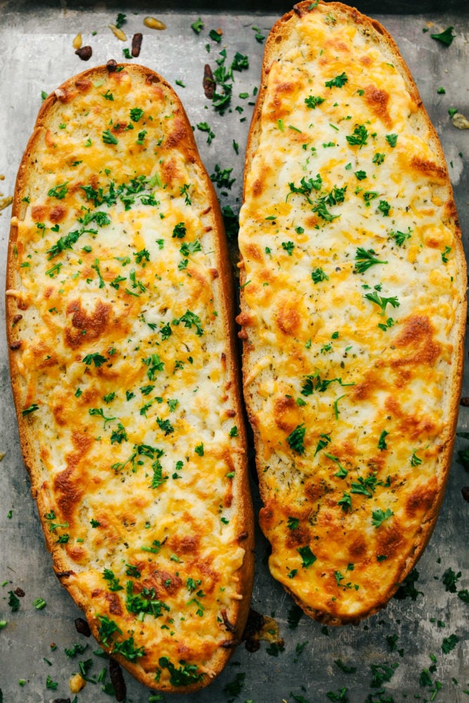 Cheesy garlic bread is so simple to make with loads of cheese and that soft bread on the inside with the crunchy crust on the outside. This is a family favorite for sure!ย Two cheesy garlic bread pieces next to each other on a pan.