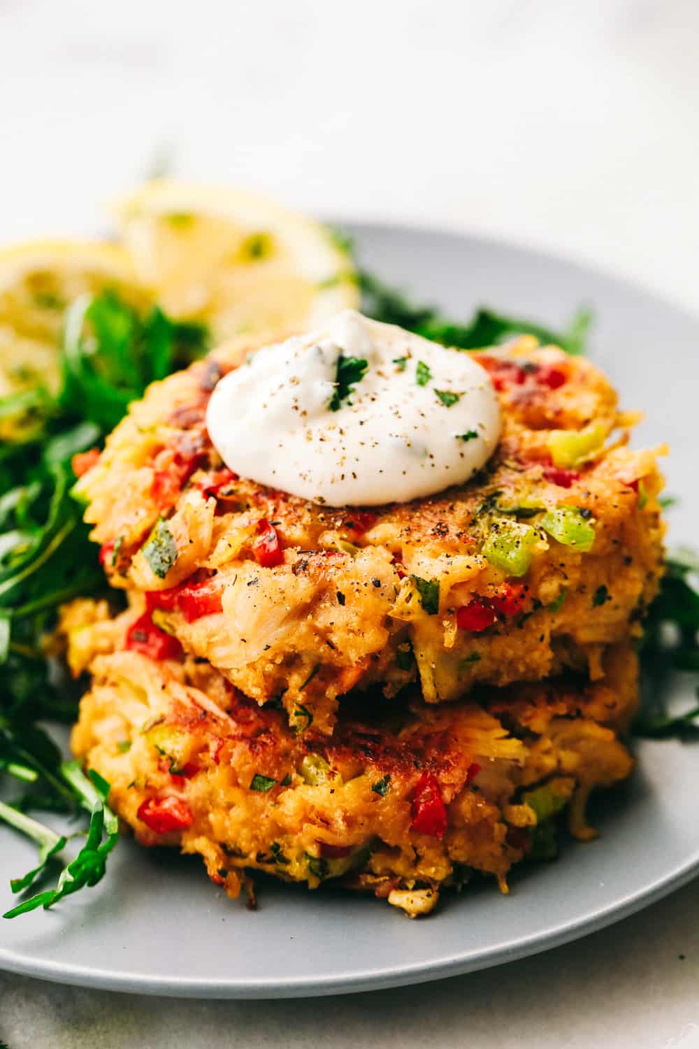 Chicken Croquettes are filled with panko, chopped redย and green bell peppers, cookedย chicken, creamy mayonnaise, seasoned with garlic powder and mixed together into small rounds. These are SO easy to make!ย Two chicken croquettes stacked on top of each other with a dollop of sauce.