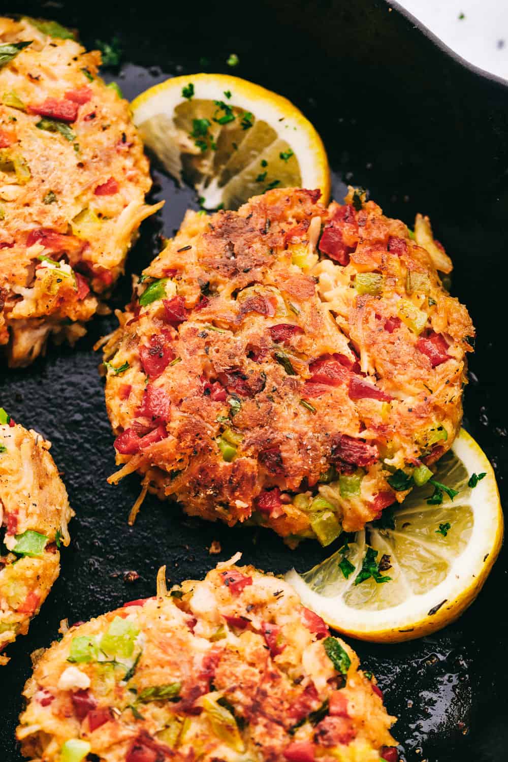 Chicken Croquettes are filled with panko, chopped redย and green bell peppers, cookedย chicken, creamy mayonnaise, seasoned with garlic powder and mixed together into small rounds. These are SO easy to make!ย Chicken croquettes on a skillet with lemon being cooked.