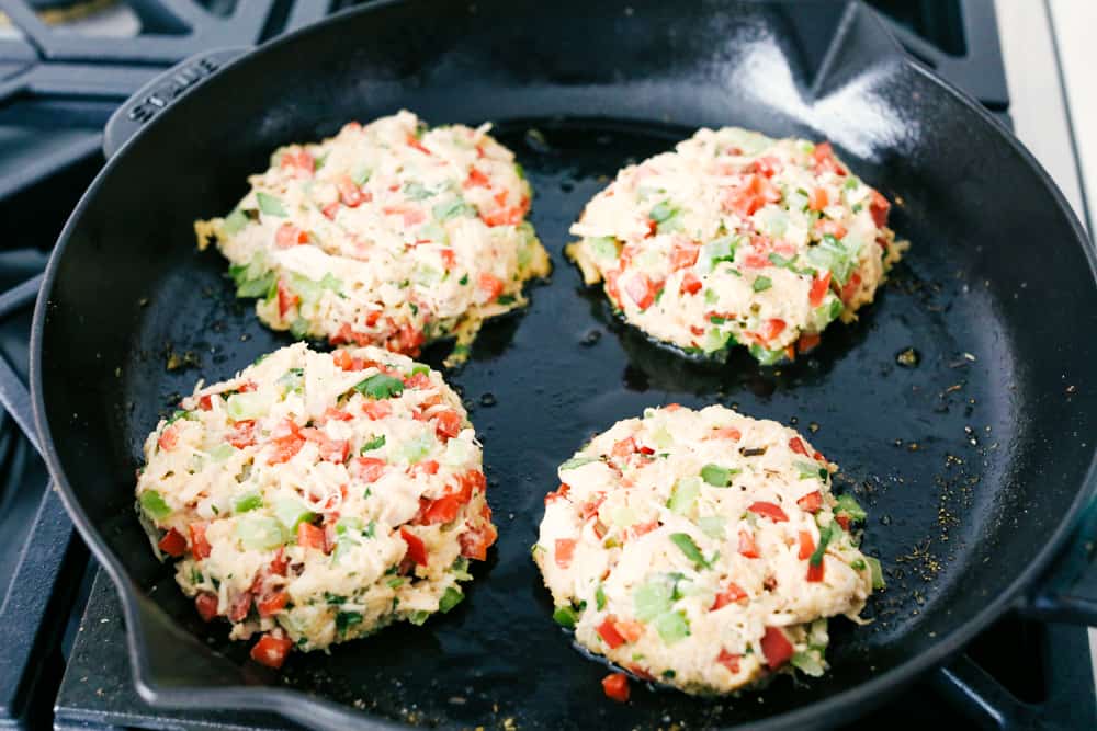 Chicken Croquettes are filled with panko, chopped redย and green bell peppers, cookedย chicken, creamy mayonnaise, seasoned with garlic powder and mixed together into small rounds. These are SO easy to make!ย Chicken croquettes on a skillet being fried.