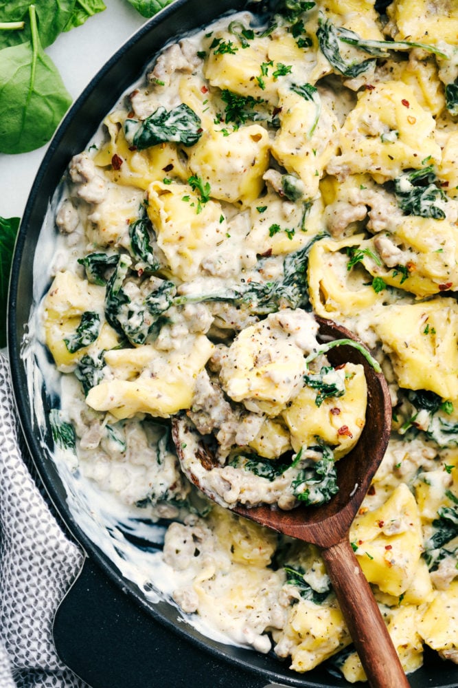 This sausage tortellini skillet is perfect for a creamy and savory dinner that is simple and tastes amazing with all the flavors blended together. It is a family favorite!ย Creamy sausage tortellini skillet cooked together in a skillet with a wooden spoon stirred through.