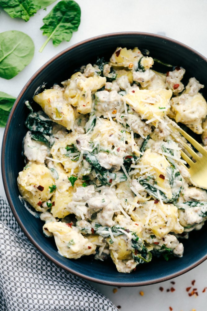 This sausage tortellini skillet is perfect for a creamy and savory dinner that is simple and tastes amazing with all the flavors blended together. It is a family favorite!ย Sausage tortellini in a bowl with a fork and garnished with shredded parmesan.