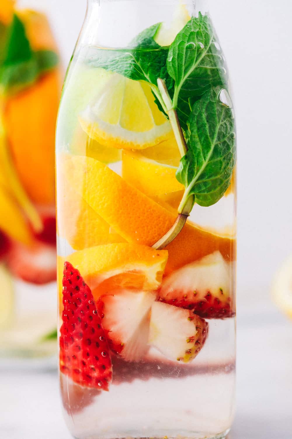 Detox Water is a naturally flavored water mixed with sliced oranges,ย citrus filled lemons and limes, fresh strawberries and garnished with mint making this anย irresistibleย water. Only 5 Minutes to make!ย Up close photo of a glass jar with oranges, strawberries, mint and cucumbers.