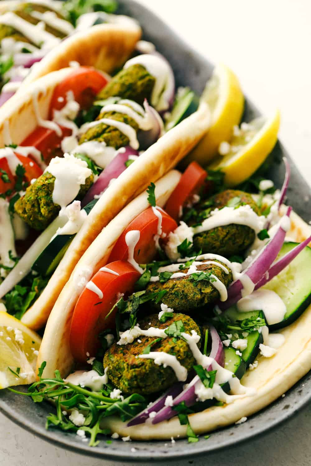 Falafel is a round bite sized mixture of garbanzo beans, seasonings and a hint of spice from a jalapeño all cooked and ready to add to any wrap or salad. A healthy little bite! Falafel on a wrap with onions and tomatoes with lemon garnish.