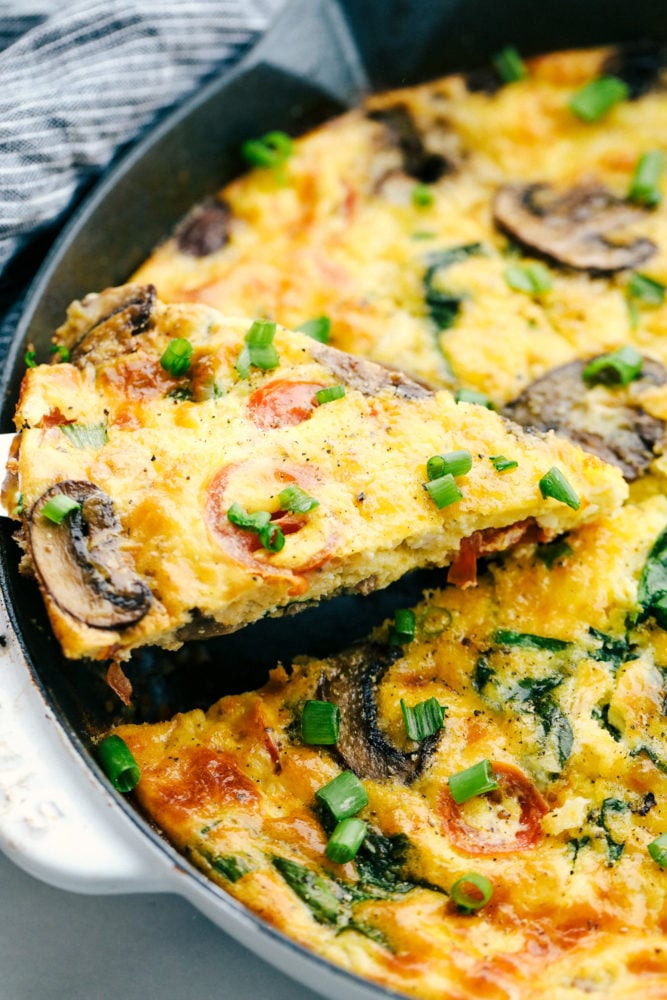 This breakfast frittata is filled with chunks of sausage, slices of mushrooms and sweet tomatoes making this a breakfast everyone will love. So simple to make and full of so much flavor! Lifting a slice of frittata out of the skillet.