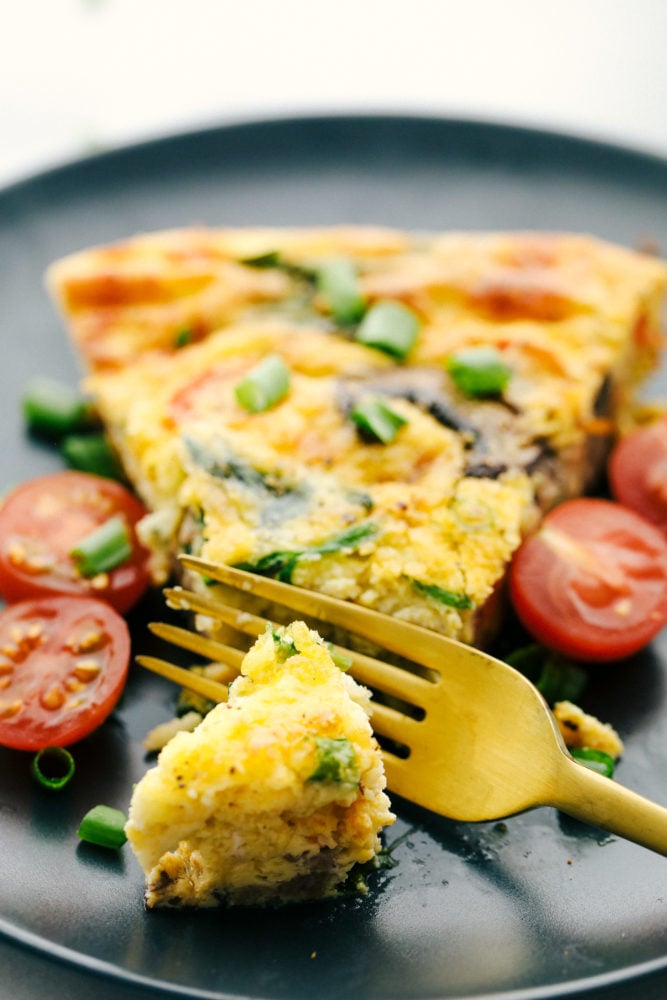 This breakfast frittata is filled with chunks of sausage, slices of mushrooms and sweet tomatoes making this a breakfast everyone will love. So simple to make and full of so much flavor! Sausage and mushroom frittata on a plate with a piece cut off with sliced cherry tomatoes on the side.
