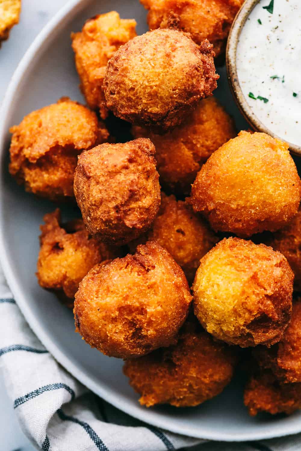 Southern Hush Puppies are golf ball sized, light and flakey cornmeal dough that is fried golden brown on the outside and soft on the inside served as a side dish to any southern meal. These hush puppies are ready in minutes! Hush puppies on a plate with a side of tartar sauce.