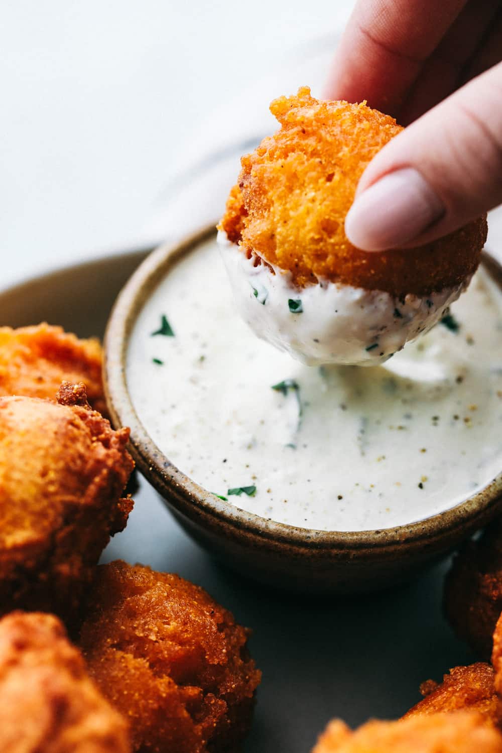 Southern Hush Puppies are golf ball sized, light and flakey cornmeal dough that is fried golden brown on the outside and soft on the inside served as a side dish to any southern meal. These hush puppies are ready in minutes! Hush puppies being dipped in tartar sauce.