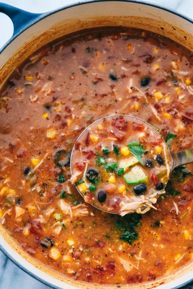 You are going to fall in love with this quick and easy 8 Can Chicken Taco Soup recipe! It is the perfect dinner when there is no time to run to the grocery store but the family needs dinner, like, NOW. Grab these ingredients right out of your pantry and whip up a delicious and flavorful soup! All 8 cans of ingredients in the taco chicken soup cooking in a pot with a ladle showing the ingredients cooking together.