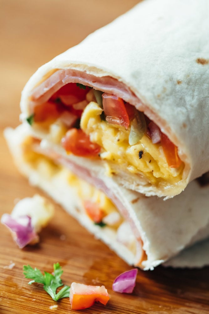 These breakfast burritos are freezer friendly and stuffed with scrambled eggs, deli ham, pico de gallo and plenty of cheese. Breakfast burritos stacked on top of each other