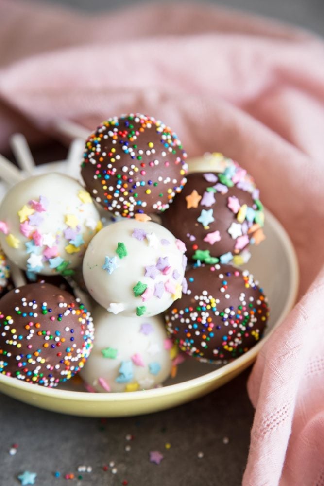 Cake Pops are the cutest desserts for any celebratory occasions. These pretty cake pops are made with vanilla cake mixed with cream cheese frosting, covered with melted chocolate and festive sprinkles. Cake pops in a bowl