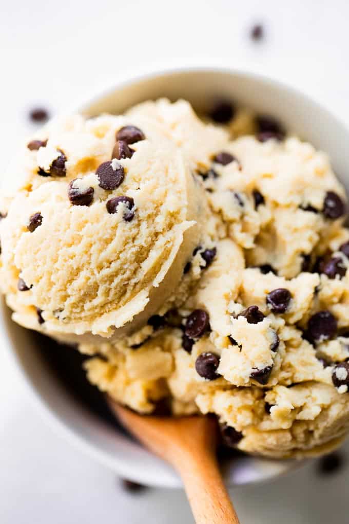 This edible cookie dough will definitely hit the spot. No need to steal those risky bites of cookie dough anymore, make an entire bowl of this safe to eat cookie dough! Edible cookie dough in a white bowl with a wooden spoon.