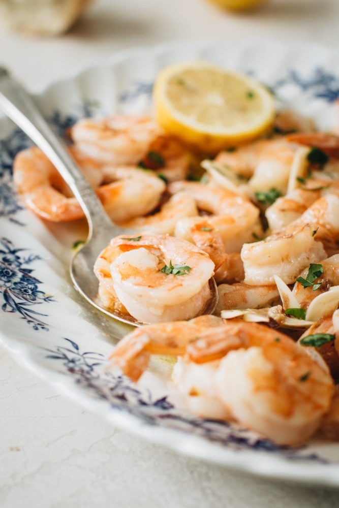Classic Shrimp Scampi is a delicious recipe of pan-cooked shrimp drenched in decadent garlic butter and lemon sauce. This simple shrimp dish is made in minutes and is best served over pasta or with crusty bread for dipping. shrimp on blue and white plate