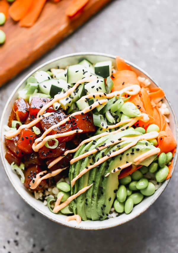 This easy Poke Bowl Recipe ย is packed with sushi-grade ahi tuna seasoned with soy, honey, and plenty of sesame. It's served with sticky brown rice, tons of veggies and these easiest spicy mayo on the planet.ย Poke bowl with ahi tuna, cucumbers, avocado and carrots all in a bowl.