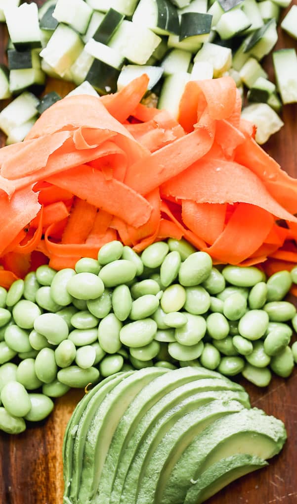 This easy Poke Bowl Recipe ย is packed with sushi-grade ahi tuna seasoned with soy, honey, and plenty of sesame. It's served with sticky brown rice, tons of veggies and these easiest spicy mayo on the planet.ย Fruits and vegetables cut up and put in order from zucchini, carrots, peas and avocado.