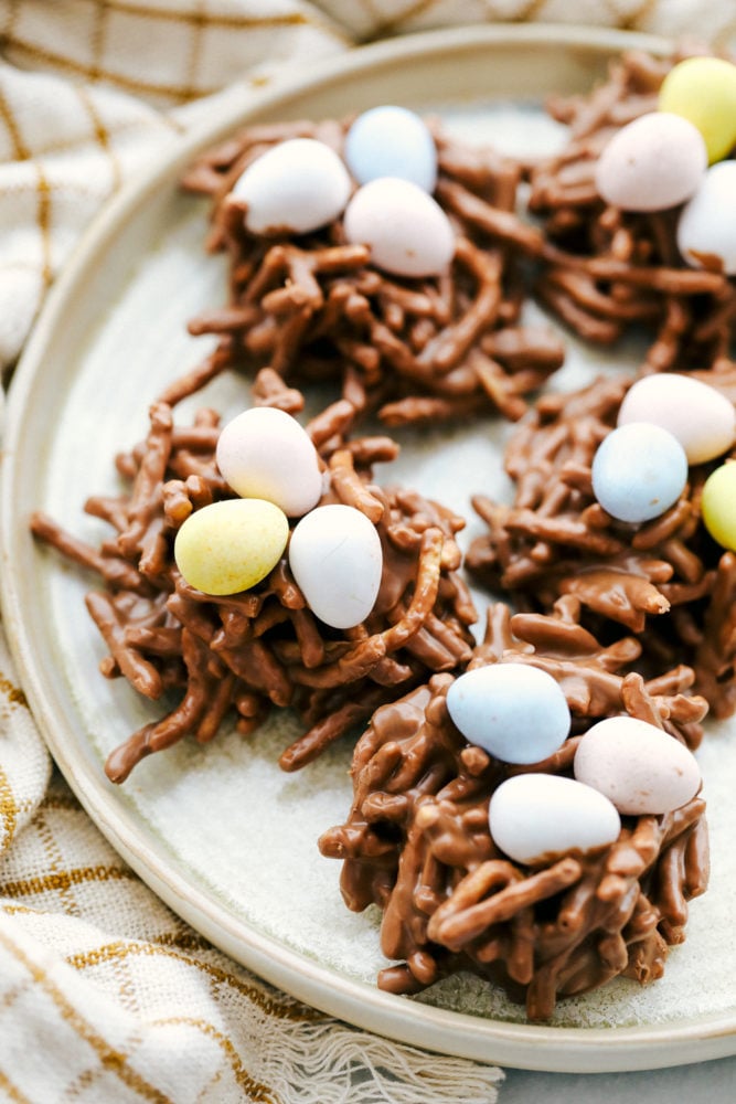 These birds nest cookies are so cute, little and fun to make with kiddos. They are filled with creamy peanut butter, milk chocolate and butterscotch chips all melted together with chow Mein noodles to look like a nest. Add Cadbury eggs for a special touch birds nest touch! A plate full of birds nest with Cadbury eggs on top.