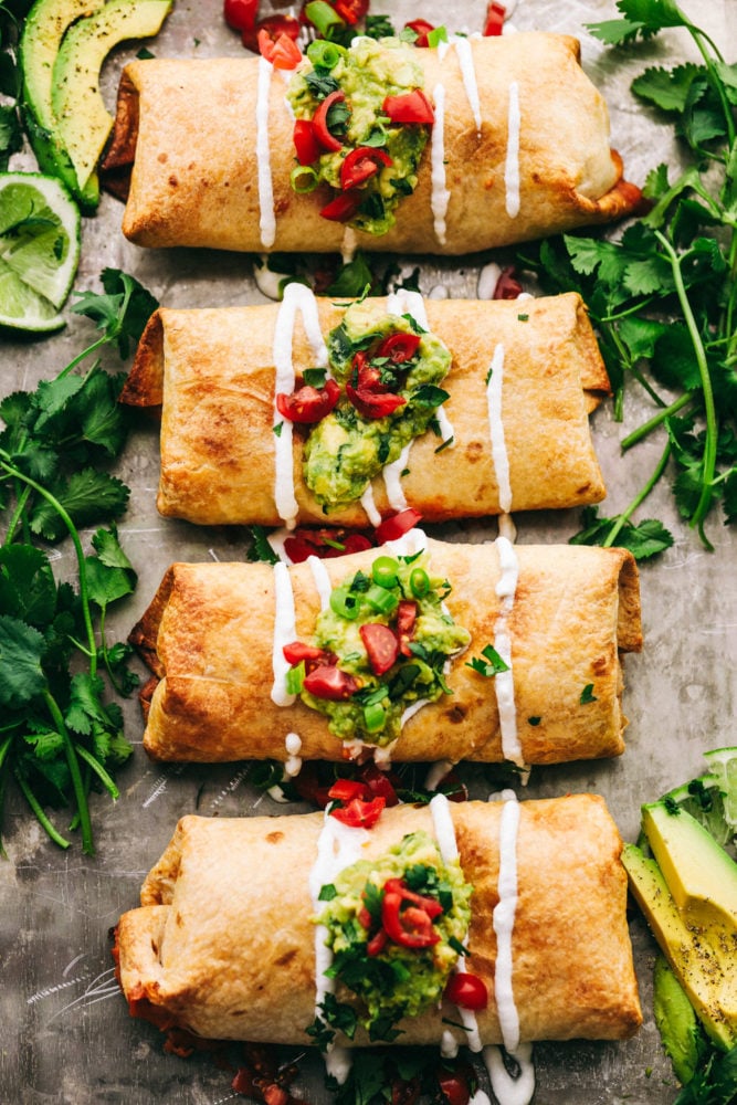 Try these chimichangas either baked or pan fried with tender chicken, stuffed Mexican filling all wrapped in a soft but crispy crust on the outside. These will become a family favorite! Four chicken enchilada lined up with guacamole, tomatoes and seasoning over top.