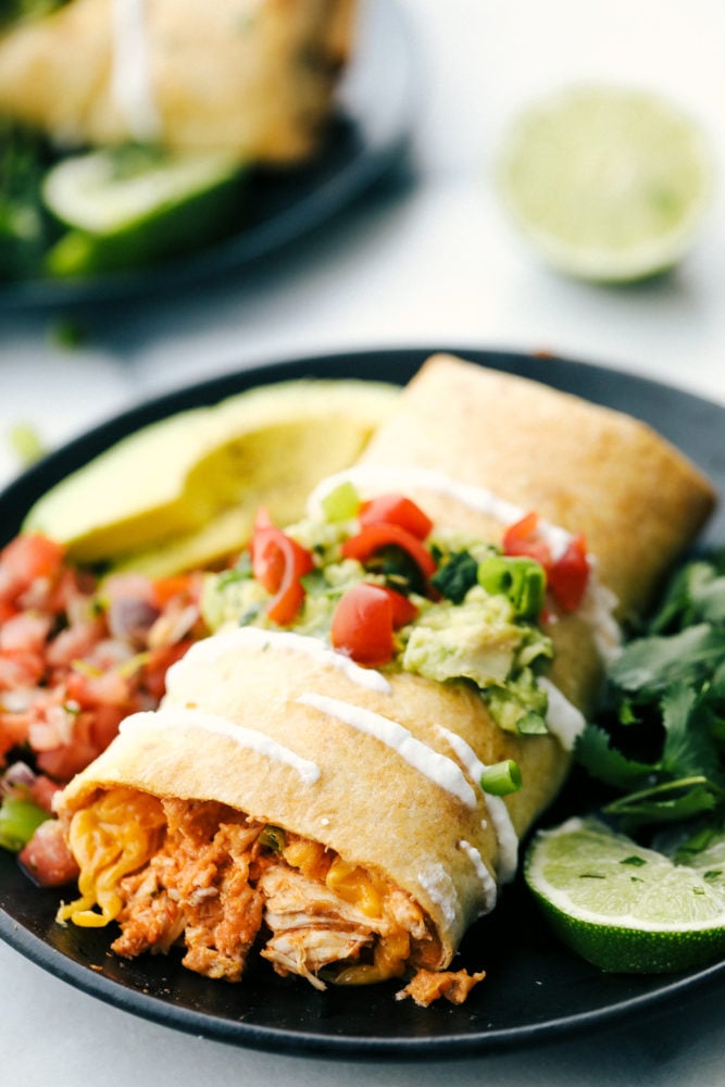 Try these chimichangas either baked or pan fried with tender chicken, stuffed Mexican filling all wrapped in a soft but crispy crust on the outside. These will become a family favorite! Chicken chimichanga on a plate with salsa, avocado and limes.