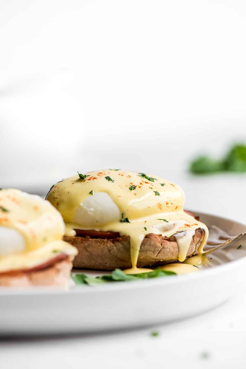 Eggs Benedict is a breakfast favorite! An English muffin is topped with Canadian bacon, a poached egg, and then drizzled with buttery hollandaise sauce. Your next brunch needs this! Eggs Benedict on a plate with the the hollandaise sauce dropping off the poached eggs.
