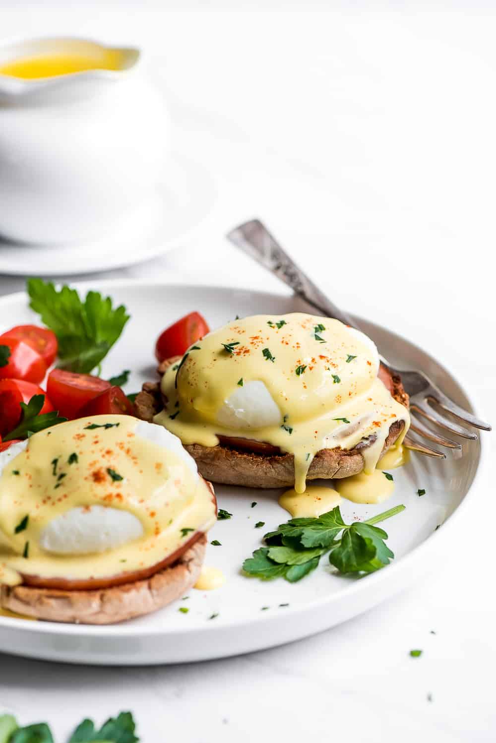 Eggs Benedict is a breakfast favorite! An English muffin is topped with Canadian bacon, a poached egg, and then drizzled with buttery hollandaise sauce. Your next brunch needs this! Two Eggs Benedict on a plate with hollandaise dripping off of them.