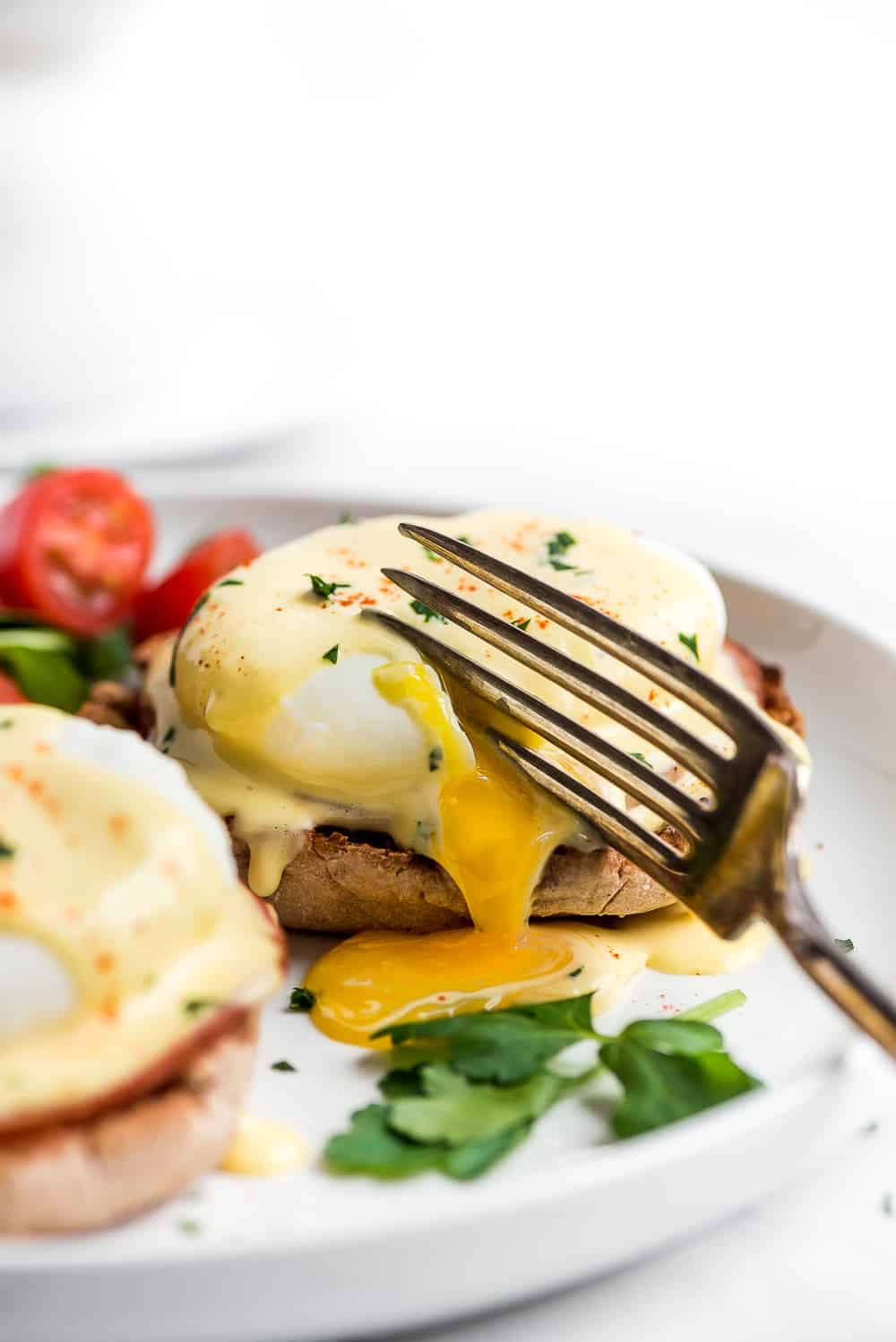 Eggs Benedict is a breakfast favorite! An English muffin is topped with Canadian bacon, a poached egg, and then drizzled with buttery hollandaise sauce. Your next brunch needs this! Egg Benedict on a plate being cut into with a fork.