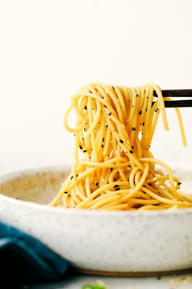 A quick and easy garlic sesame noodle recipe that is light and tasty! Add in vegetables and protein to enhance this oriental dish or keep it simple with a garlic sesame flavoring.ย Garlic sesame noodles in a bowl being pulled up with chopsticks.