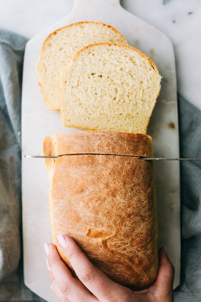 This homemade bread is always a family favorite and can be done so easily with this perfect recipe my grandma handed down to me. Making bread is easier than you think! Overhead photo of a bread loaf being sliced with a knife.