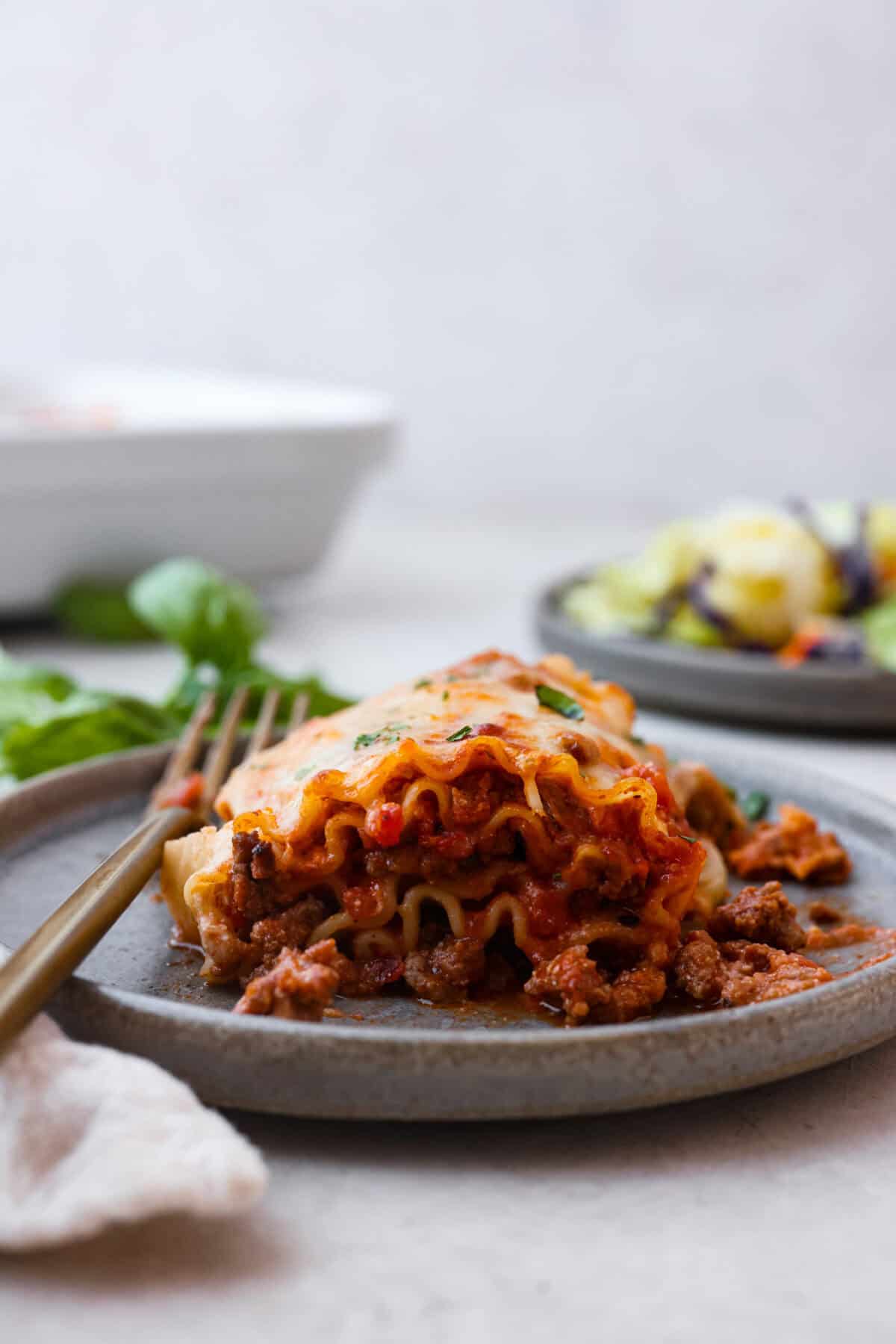 These Lasagna roll-ups have all the flavors of a classic lasagna wrapped up in a fun lasagna twist! This recipe is an easier approach to this classic Italian comfort food; seasoned beef, sweet marinara sauce, and melty, creamy cheese wrapped in a perfectly al dente noodle. Side shot of plated lasagna roll up.