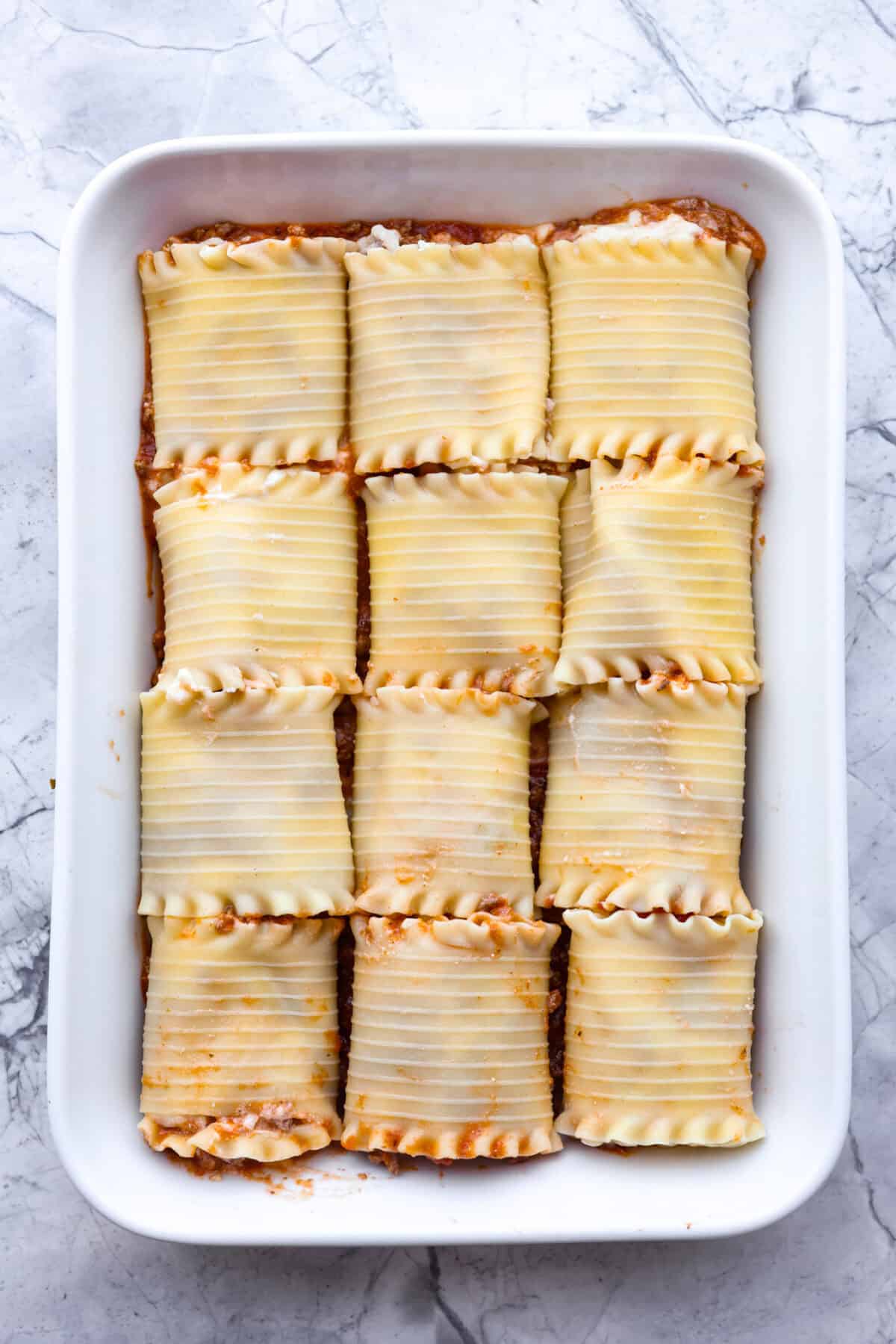 These Lasagna roll-ups have all the flavors of a classic lasagna wrapped up in a fun lasagna twist! This recipe is an easier approach to this classic Italian comfort food; seasoned beef, sweet marinara sauce, and melty, creamy cheese wrapped in a perfectly al dente noodle. Overhead shot of lasagna roll ups in baking dish.