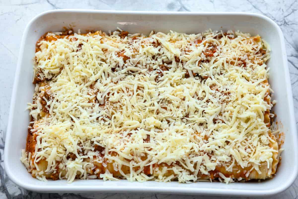 These Lasagna roll-ups have all the flavors of a classic lasagna wrapped up in a fun lasagna twist! This recipe is an easier approach to this classic Italian comfort food; seasoned beef, sweet marinara sauce, and melty, creamy cheese wrapped in a perfectly al dente noodle. Overhead shot of lasagne roll ups in backing dish with sauce and cheese spread on top.