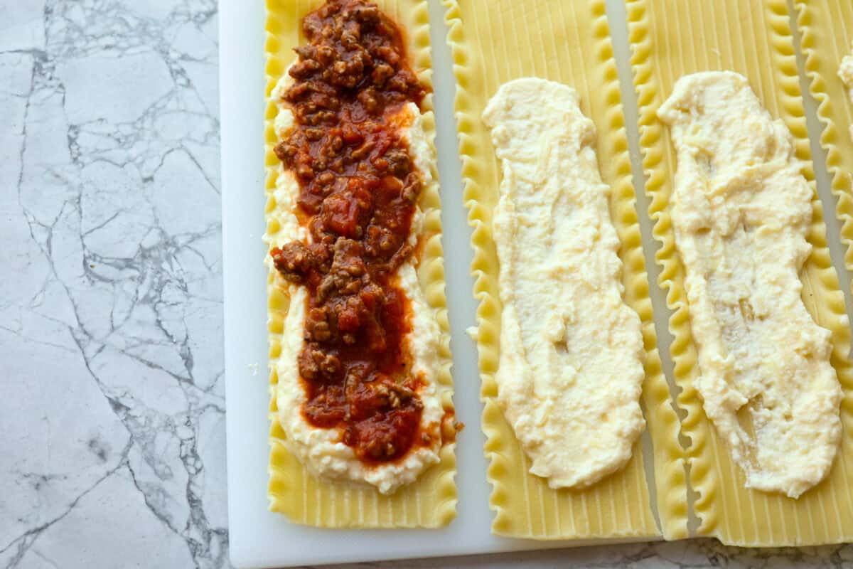 These Lasagna roll-ups have all the flavors of a classic lasagna wrapped up in a fun lasagna twist! This recipe is an easier approach to this classic Italian comfort food; seasoned beef, sweet marinara sauce, and melty, creamy cheese wrapped in a perfectly al dente noodle. Overhead shot of meat and sauce mixture spread over cheese on individual lasagna noodles.
