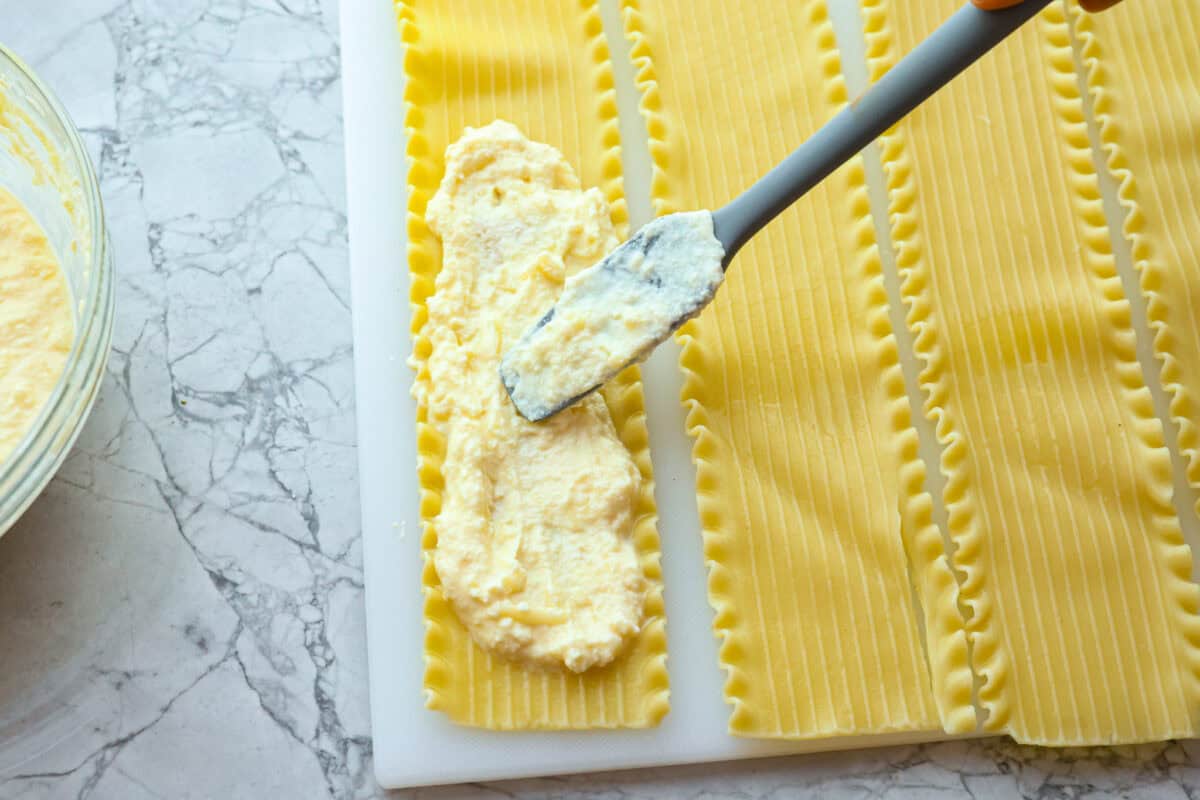These Lasagna roll-ups have all the flavors of a classic lasagna wrapped up in a fun lasagna twist! This recipe is an easier approach to this classic Italian comfort food; seasoned beef, sweet marinara sauce, and melty, creamy cheese wrapped in a perfectly al dente noodle. Overhead shot of cheese mixture being spread on individual lasagna noodles.