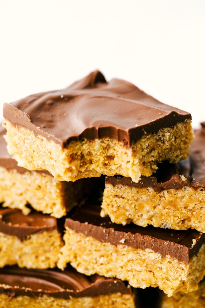 Scotcharoos are a perfect combination of butterscotch and peanut butter with a twist of a Rice Krispie crunch in the middle and a thick, rich chocolate layer that makes an irresistible treat. Sink your teeth in these ooey gooey bars! Scotcharoos stacked on top of each other and one has a teeth marks on top.