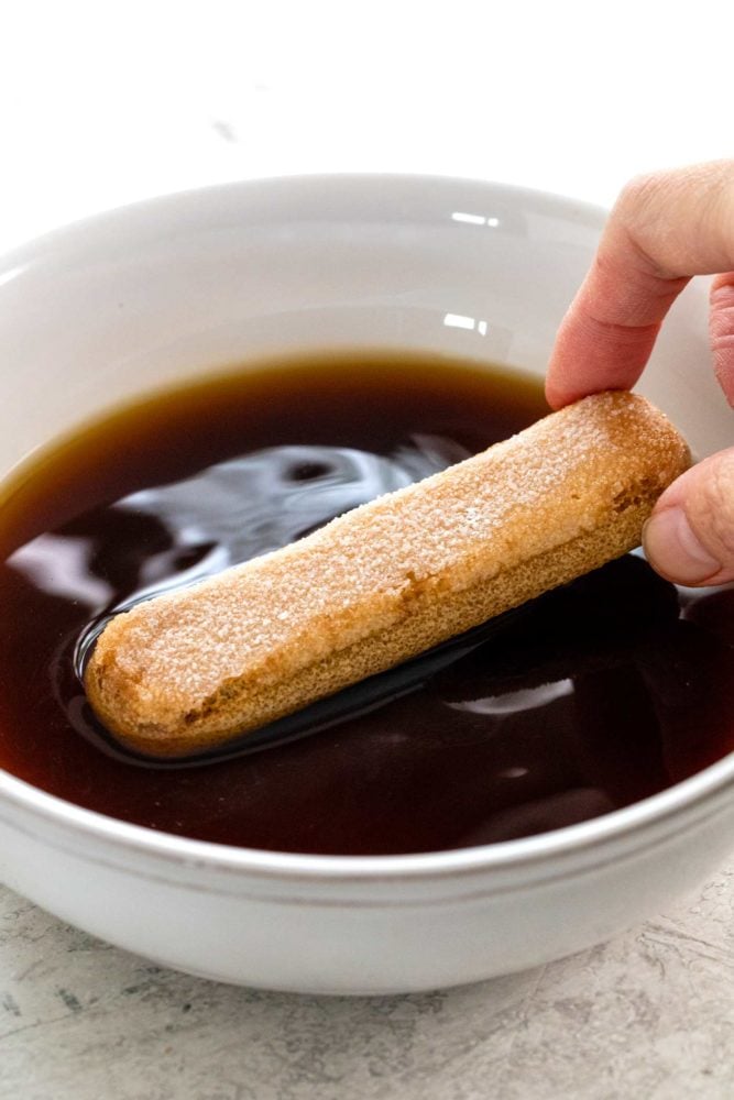 Tiramisu is a popular no-bake Italian dessert meant to feed a crowd. Ladyfinger cookies are dipped in coffee then layered with a sweetened mascarpone cheese filling. The final touch is a sprinkling of cocoa powder on top. soaking a ladyfinger cookie in a bowl of coffee