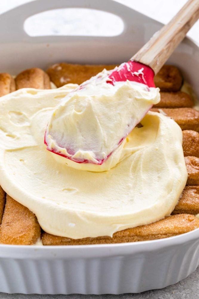 Tiramisu is a popular no-bake Italian dessert meant to feed a crowd. Ladyfinger cookies are dipped in coffee then layered with a sweetened mascarpone cheese filling. The final touch is a sprinkling of cocoa powder on top. spreading filling mixture on ladyfingers sitting in a baking dish
