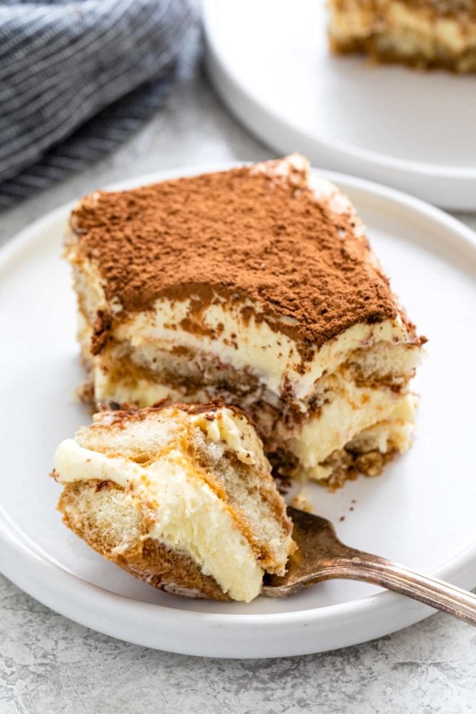 Tiramisu is a popular no-bake Italian dessert meant to feed a crowd. Ladyfinger cookies are dipped in coffee then layered with a sweetened mascarpone cheese filling. The final touch is a sprinkling of cocoa powder on top. Slice of tiramisu on a plate with a spoonful taken out