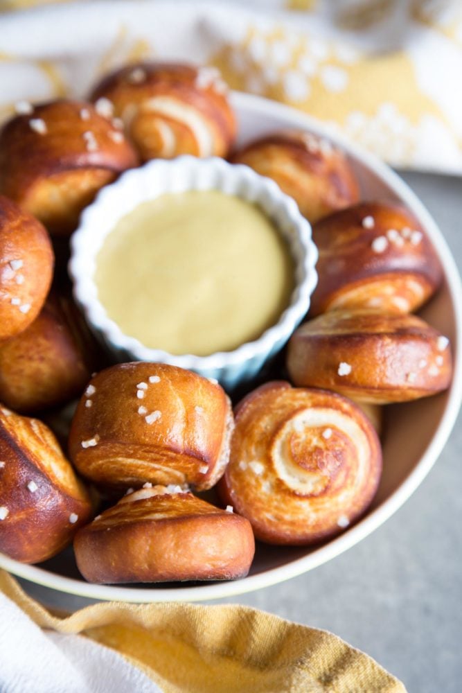 Pretzel Bites are the perfect afterschool snacks, game day appetizers, and popcorn replacement for movie nights. The outside of each pretzel bites is golden brown and chewy, while the inside is soft and fluffy. Pretzel bites in a bowl with a cup of mustard