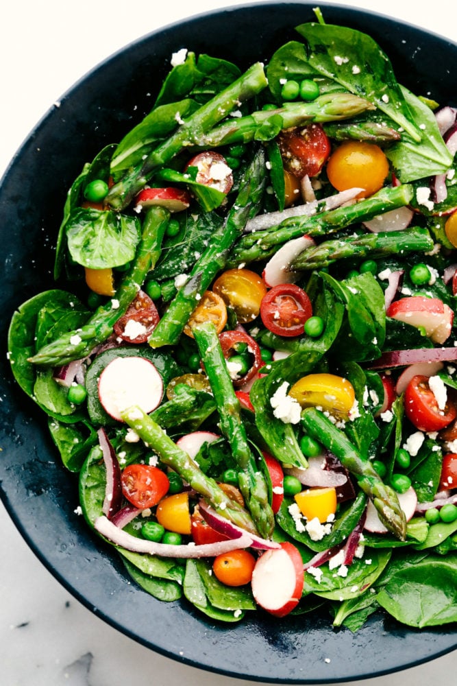 This fresh asparagus salad is one of my favorites and I can't wait to show you how to make it. With lemon vinaigrette dressing drizzled on top this salad has a light and flavorful crisp crunch in every bite. Asparagus salad with tomatoes, radish and spinach in a black bowl.