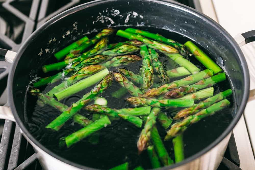 This fresh asparagus salad is one of my favorites and I can't wait to show you how to make it. With lemon vinaigrette dressing drizzled on top this salad has a light and flavorful crisp crunch in every bite. Asparagus cooking in boiling water on a gas stove top.