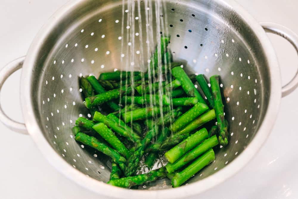 This fresh asparagus salad is one of my favorites and I can't wait to show you how to make it. With lemon vinaigrette dressing drizzled on top this salad has a light and flavorful crisp crunch in every bite. Asparagus being washed with cold water in a strainer.