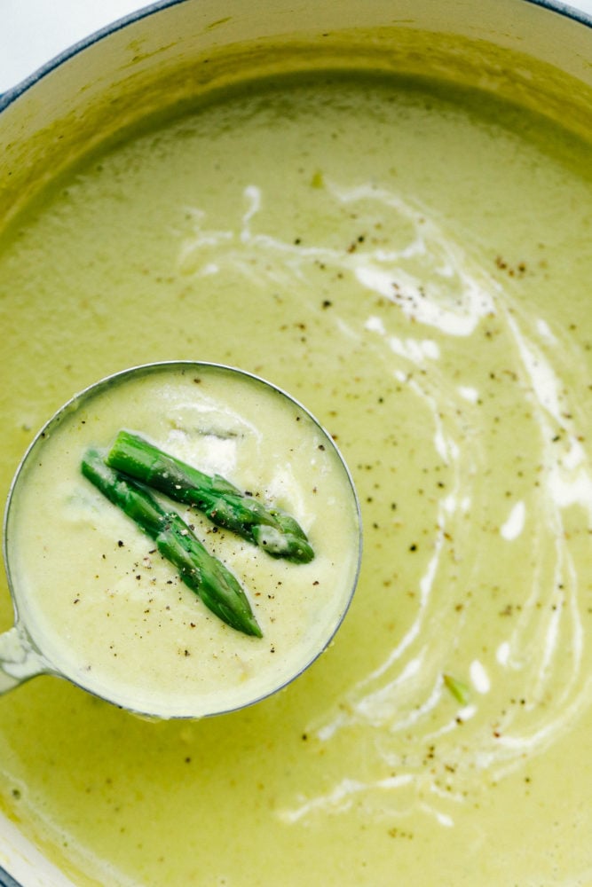 This asparagus soup is rich, flavorful and creamy not to mention it is simple to make! The velvety texture melts in your mouth leaving you wanting more. Asparagus soup in a pot with a ladle full of asparagus soup and two asparagus tips.