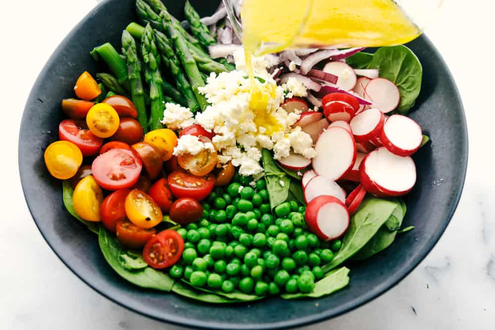 This fresh asparagus salad is one of my favorites and I can't wait to show you how to make it. With lemon vinaigrette dressing drizzled on top this salad has a light and flavorful crisp crunch in every bite. All the ingredients separated in a bowl with the lemon vinaigrette being poured over top.