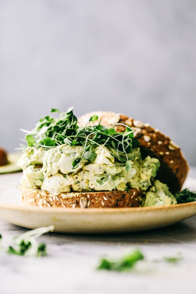 Avocado egg salad is a twist on egg salad adding in the avocado for the color and delicious flavor! Add this to any sandwich or eat it straight from the bowl, it will be a new favorite! Avocado egg salad on a sandwich with Brussel sprouts.