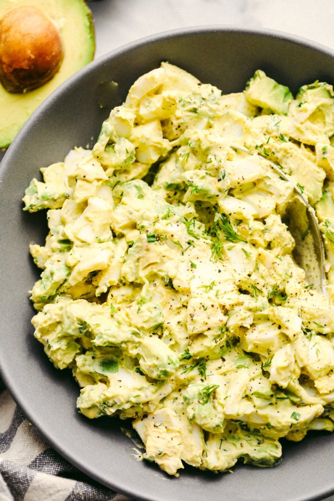 Avocado egg salad is a twist on egg salad adding in the avocado for the color and delicious flavor! Add this to any sandwich or eat it straight from the bowl, it will be a new favorite! Avocado egg salad mixed together in a gray bowl with a spoon inside of it.
