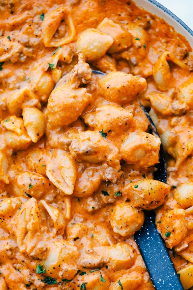 This cheesy beef and shells recipe is so simple to make with just a few ingredients straight out of your pantry, plus it all comes together in 20 minutes. Comforting, cheesy dinner that the whole family will love! Cheesy beef and shells in a skillet with a ladle stirring them up.
