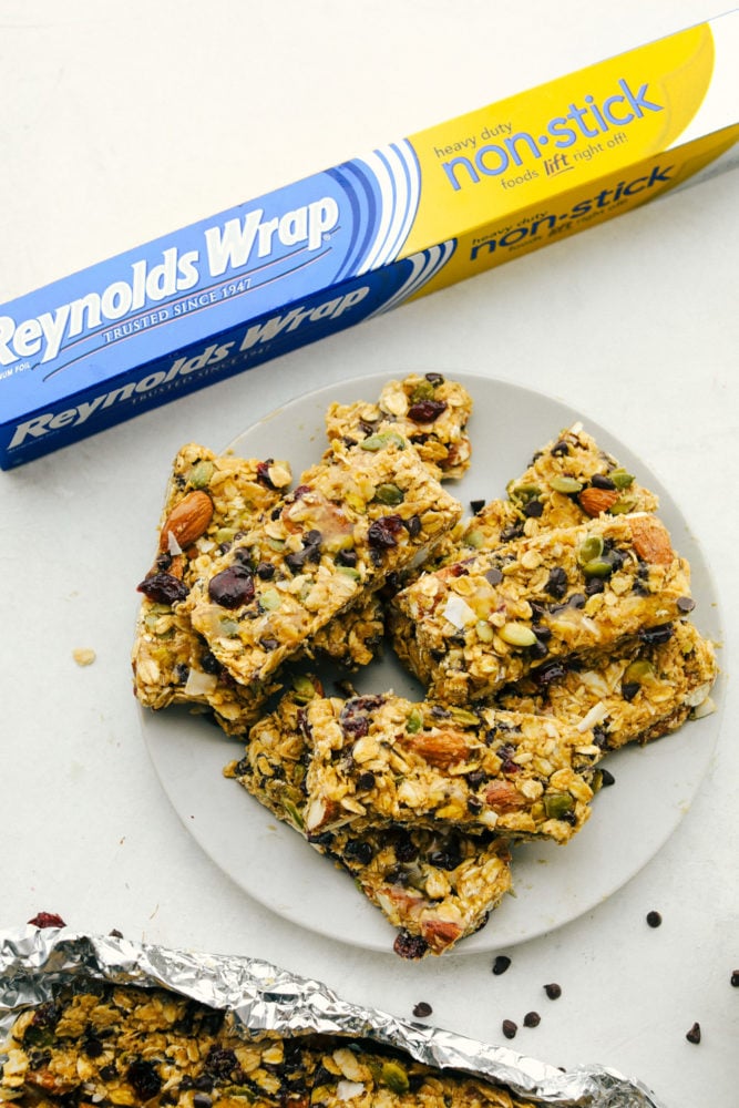 Easy to make chewy granola bars that are homemade filled with regular oats, dried cranberries, salty almonds, mini dark chocolate chips all combined with a sweet honey and a peanut butter flavoring. Snack time just got easier with these tasty bars!ย Granola bars stacked on top of each other on a plate with the nonstick wrapper in the photo.
