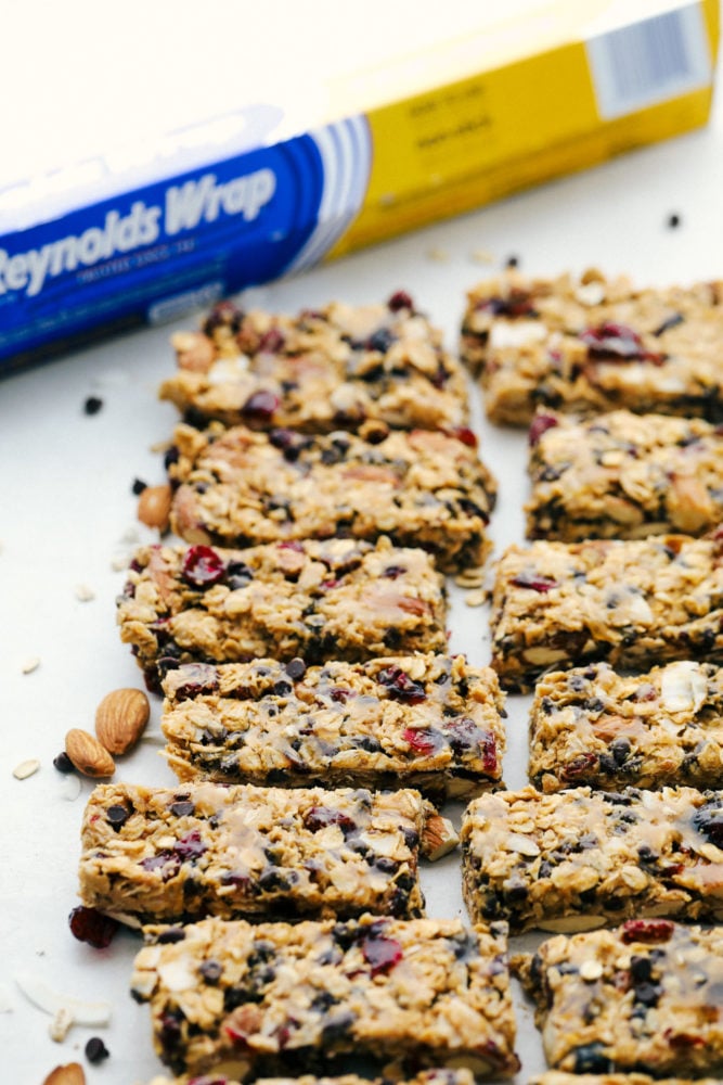 Easy to make chewy granola bars that are homemade filled with regular oats, dried cranberries, salty almonds, mini dark chocolate chips all combined with a sweet honey and a peanut butter flavoring. Snack time just got easier with these tasty bars!ย Granola bars cut into slices with the Reynolds wrap in the back ground.