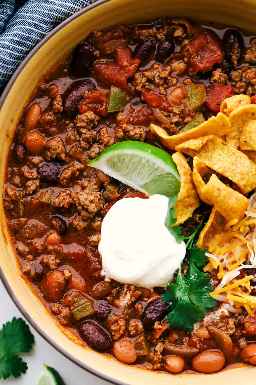 I'm telling you right now, this is the BEST chili you will ever have. The reviews don't lie! It's hearty, flavorful, and oh-so-comforting. It's packed with ground beef, beans, tomatoes, and bold spices. Get creative with your toppings and dig in! Chili in a bowl with lime wedge, sour cream, Frito chips and shredded cheese.