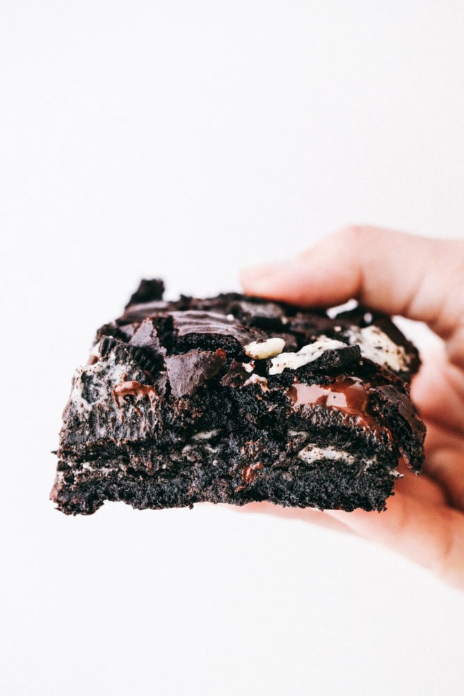These brownies are layered with a rich chocolatey batter with Oreos in the middle creating a soft, gooey center with chunks of chocolate and Oreo pieces in every bite. Oreo brownies make everyday a great day! Oreo brownie being held in the air to see the layers of oreo and batter.